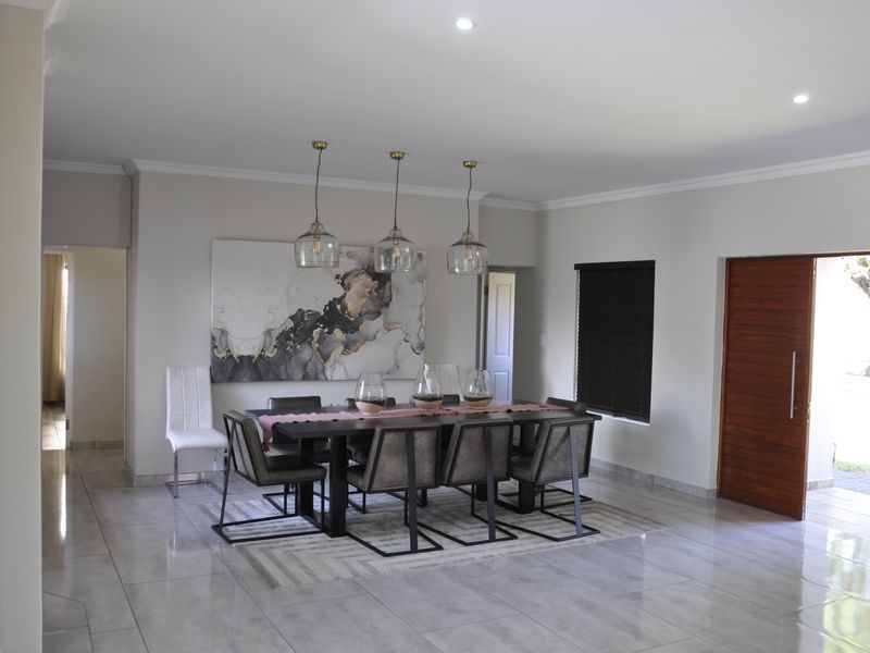 A spacious dining room featuring polished porcelain floor tiles, recessed downlighting, and a wooden sliding door leading to the exterior.