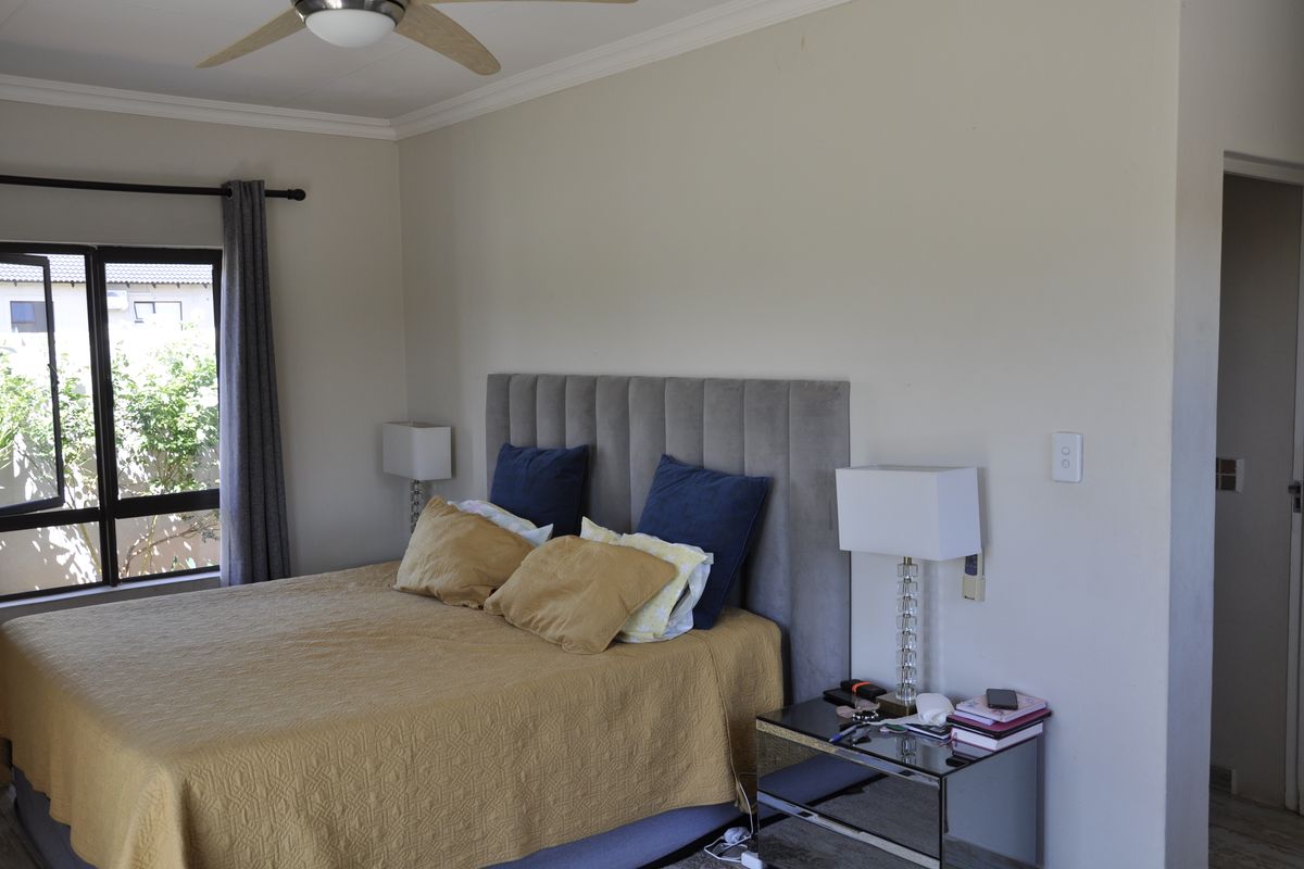 A well-maintained bedroom featuring a ceiling fan, neutral wall finishes, and large aluminium-framed windows allowing for natural light.