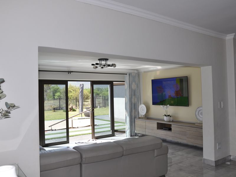 Spacious living room featuring tiled floors, crown molding, and large sliding glass doors that provide seamless access to the outdoor patio and garden area.