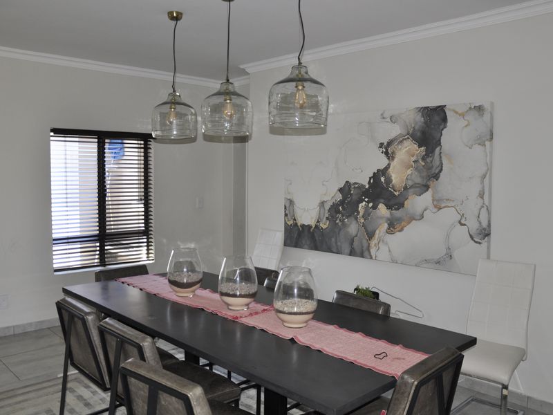 A well-maintained dining room featuring modern pendant lighting, tiled flooring, and venetian blinds, creating a bright and functional space for meals.