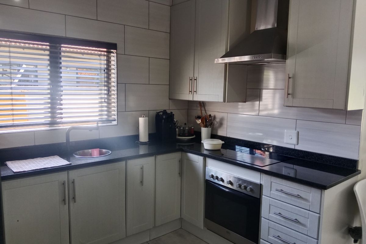 Modern kitchen featuring light-toned cabinetry, granite countertops, stainless steel built-in oven and extractor fan, and contemporary tiled backsplash.