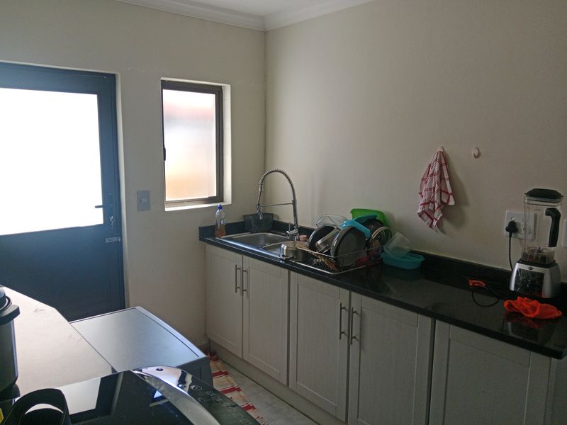 A functional scullery area featuring granite countertops, built-in cabinetry, a stainless steel sink with a modern faucet, and direct access to the exterior.