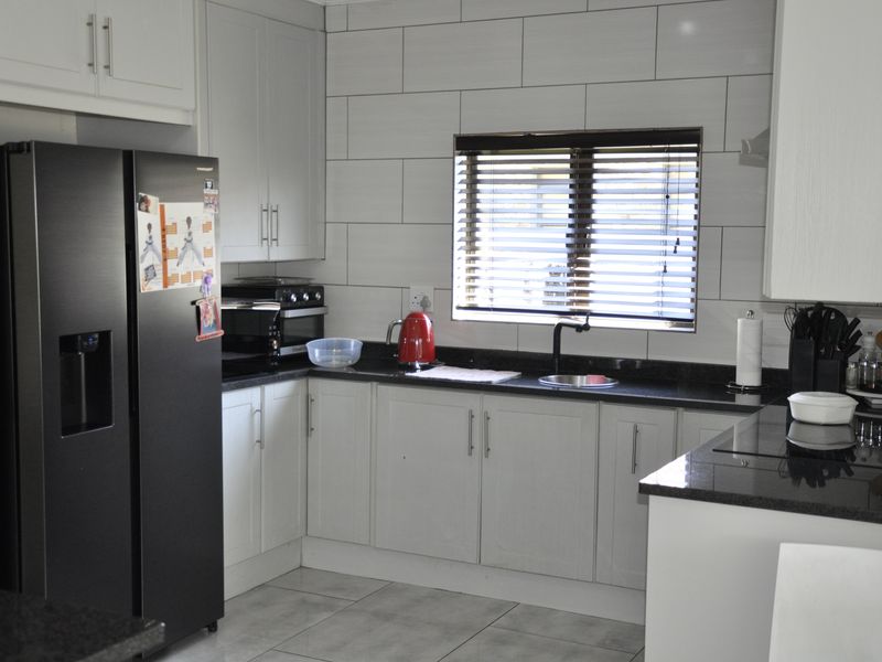 Modern kitchen featuring light grey cabinetry, dark granite countertops, subway tile backsplash, and tiled flooring with a functional layout.