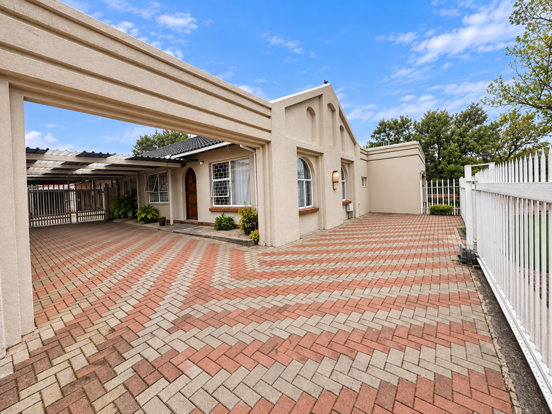 Front exterior view featuring a spacious paved driveway, covered carport, secure perimeter fencing, and well-maintained architectural facade with arched window detailing.