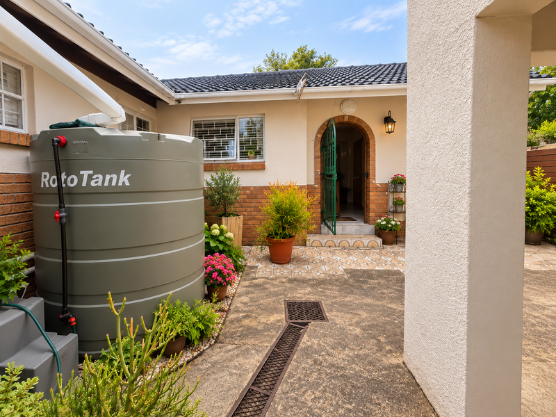 Rear courtyard area featuring a large water storage tank, brick and plaster facade, arched entrance, and functional drainage system.