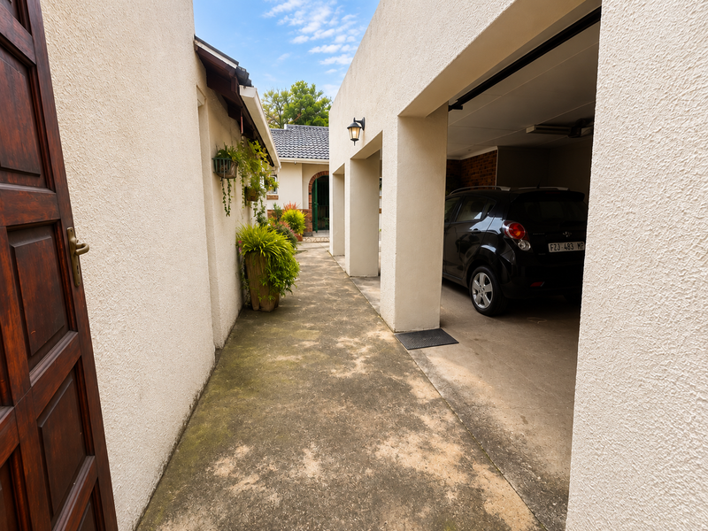 A view of the exterior driveway and covered carport area featuring stucco walls and concrete paving.