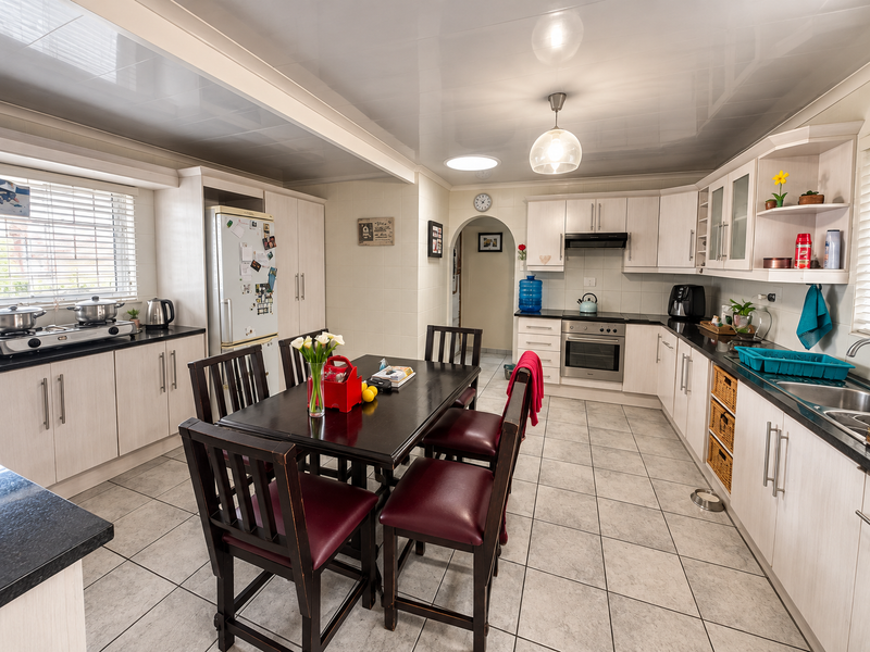 Spacious open-plan kitchen and dining area featuring light wood-finish cabinetry, dark countertops, tiled flooring, and integrated cooking appliances.
