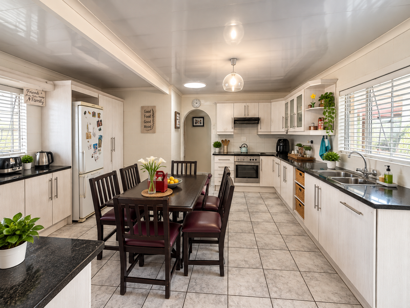 Spacious open-plan kitchen and dining area featuring light-toned cabinetry, dark countertops, ceramic tile flooring, and an integrated oven with extractor fan.