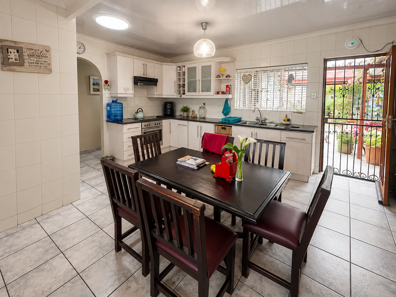 A functional kitchen featuring tiled walls and flooring, built-in cabinetry, a double basin sink, and direct access to an outdoor patio area.