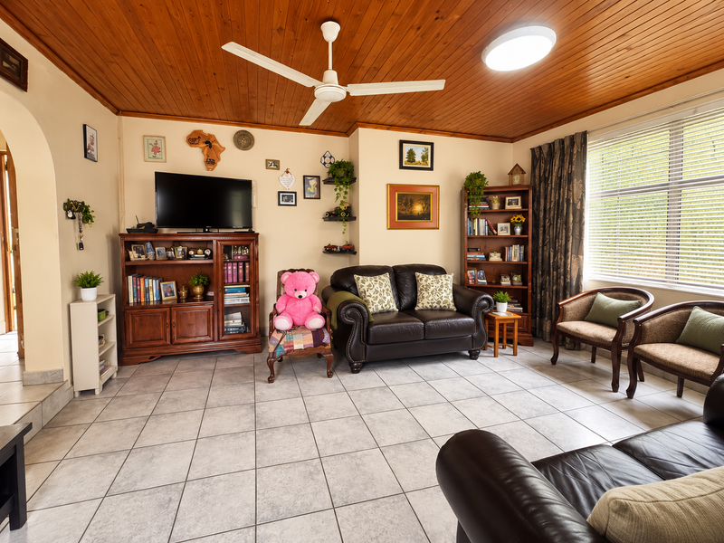 A comfortable living room featuring a warm timber tongue and groove ceiling, ceiling fan, and neutral tiled flooring with large window access.