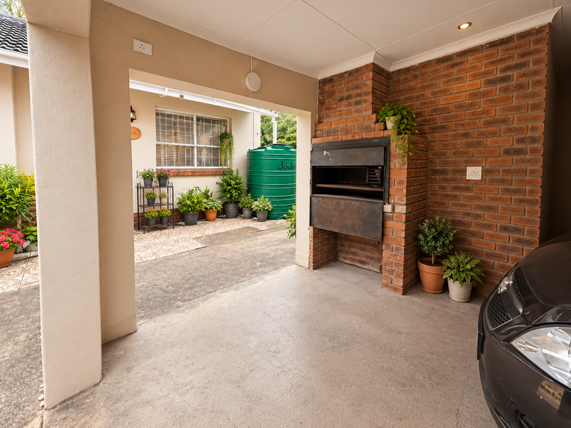Covered patio area featuring a built-in brick braai, recessed lighting, and concrete flooring, providing a functional outdoor entertainment space.