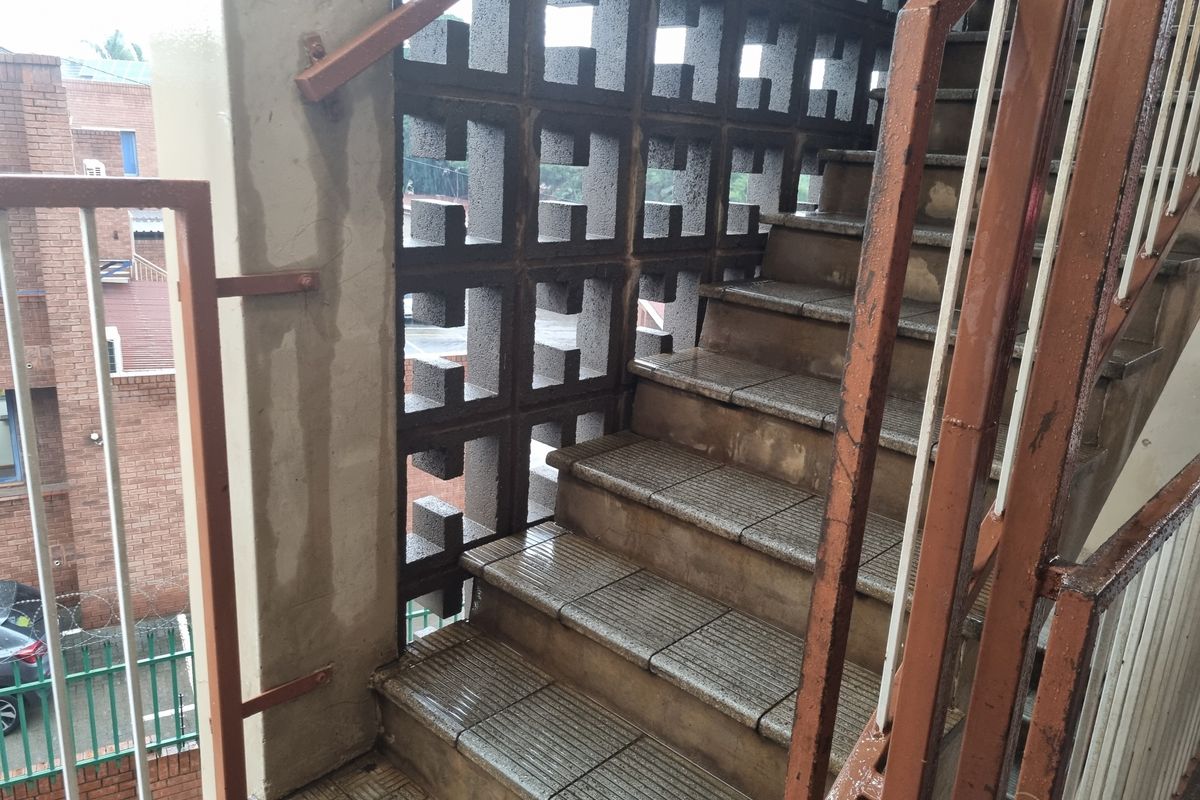 Exterior concrete staircase featuring a decorative breeze block screen wall and metal handrails, showing signs of weathering and surface corrosion.