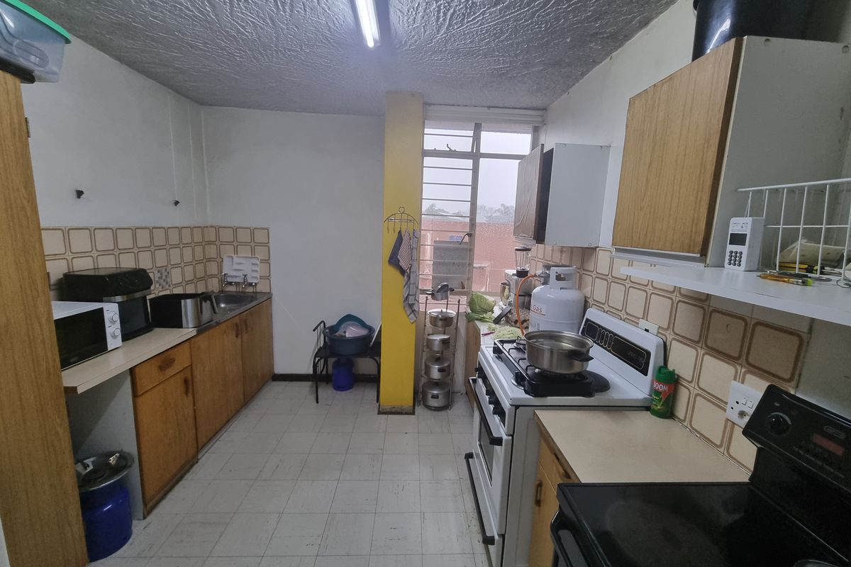 A dated kitchen featuring laminate cabinetry, tiled splashbacks, and tiled flooring, offering a functional layout with potential for modernization.