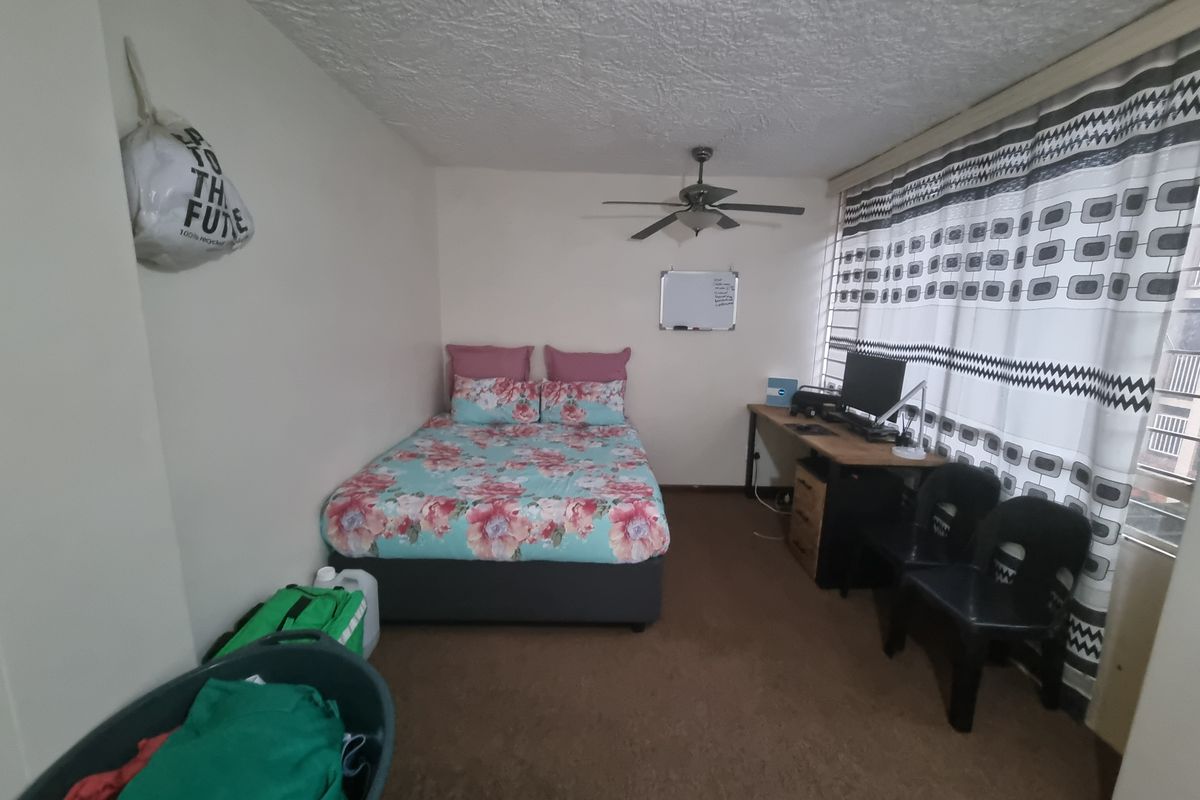 A functional bedroom featuring a ceiling fan, carpeted flooring, and a textured ceiling, offering a comfortable space for rest.