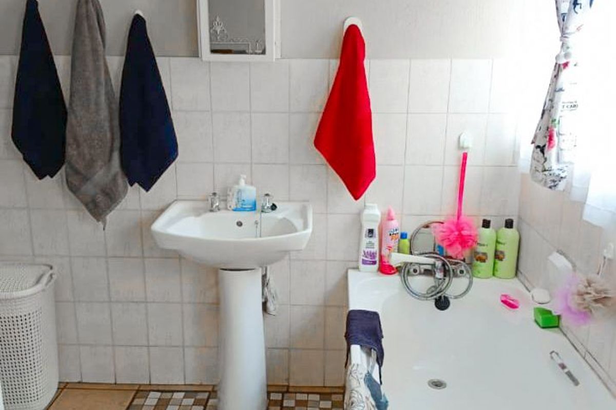 A functional bathroom featuring a pedestal basin, bathtub, and tiled splashback with neutral wall finishes and ceramic floor tiling.