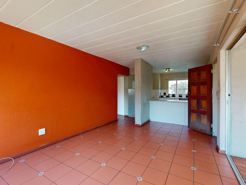 An open-plan living area featuring tiled flooring, a breakfast bar connecting to the kitchen, and a sliding glass door leading to the exterior.