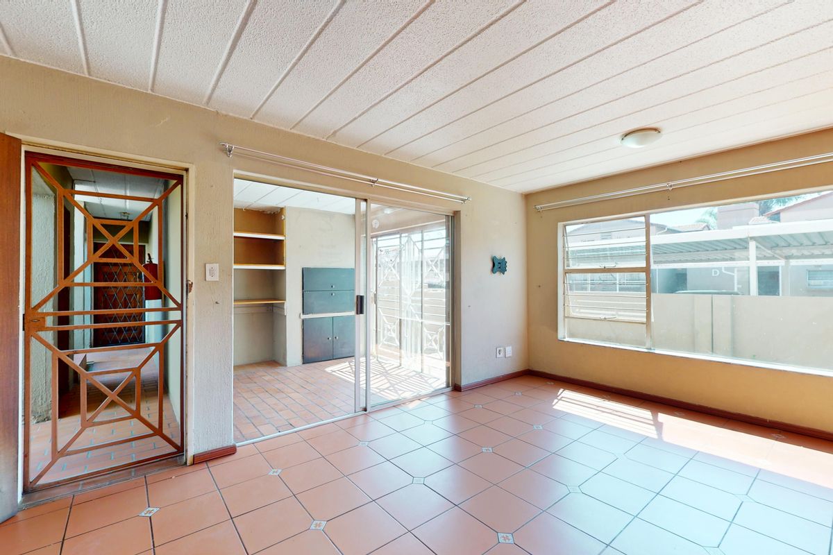 An empty living room featuring tiled flooring, large windows for natural light, and a sliding glass door leading to an adjacent utility space.
