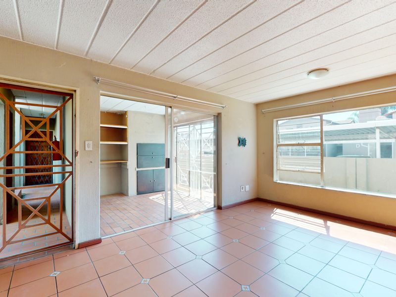 An empty living room featuring tiled flooring, large windows for natural light, and a sliding glass door leading to an adjacent utility space.