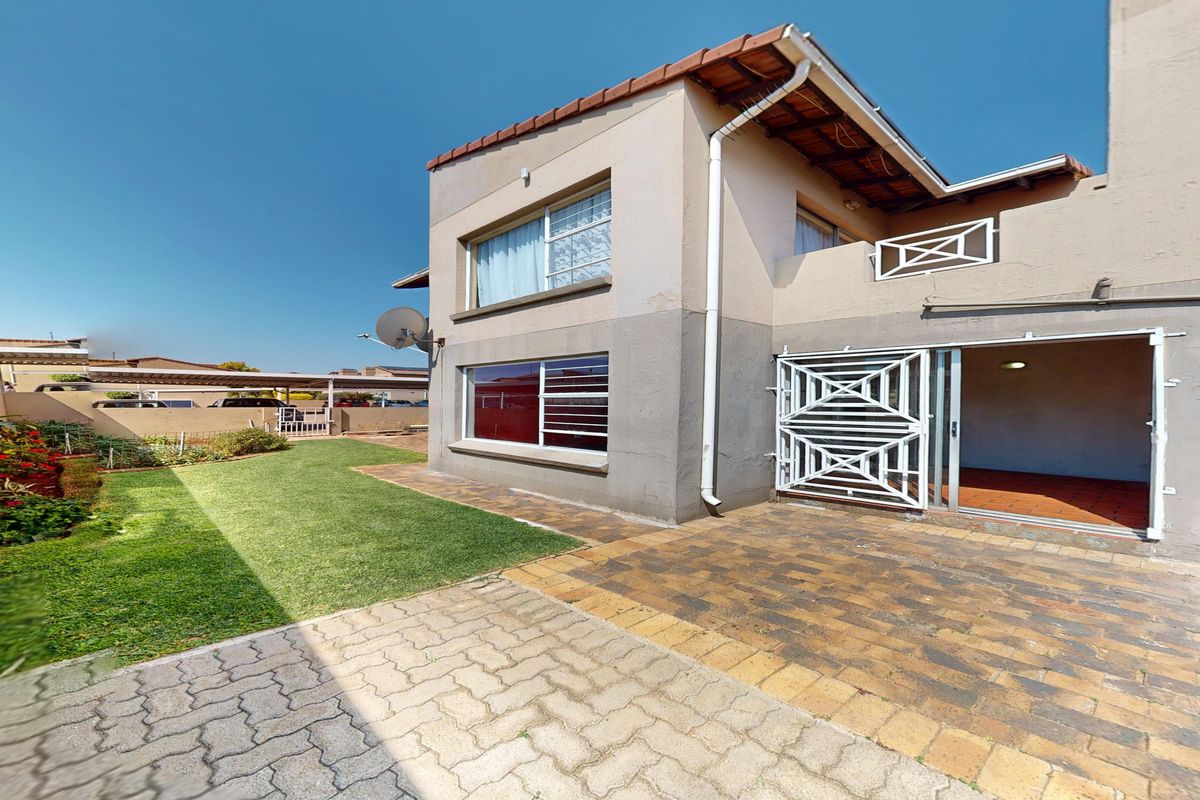 Rear view of the townhouse featuring a paved patio area, small lawn, and direct access via a sliding door with security gate.