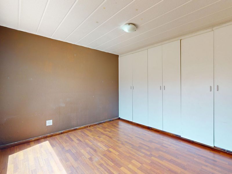 A vacant bedroom featuring laminate flooring, built-in cupboards, and a neutral ceiling, offering a blank canvas for personalization.
