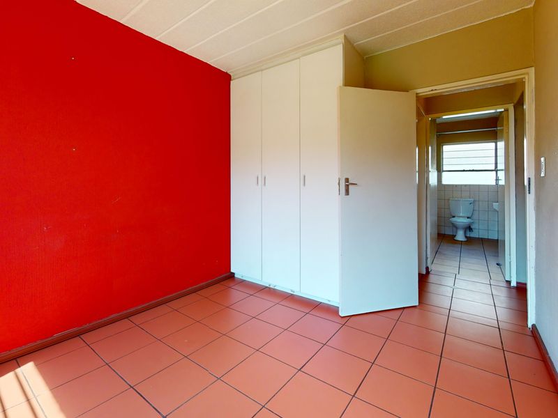 An empty bedroom featuring tiled flooring, built-in cupboards, and direct access to an en-suite bathroom.