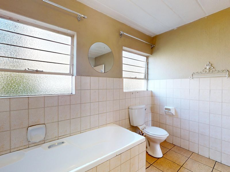 A dated bathroom featuring a standard bathtub, toilet, and tiled finishes, requiring modernization to improve its aesthetic and functionality.