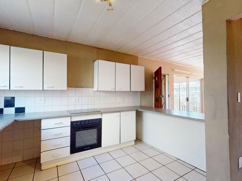 Functional kitchen featuring white cabinetry, laminate countertops, built-in oven and hob, tiled backsplash, and a breakfast bar overlooking the adjacent living area.