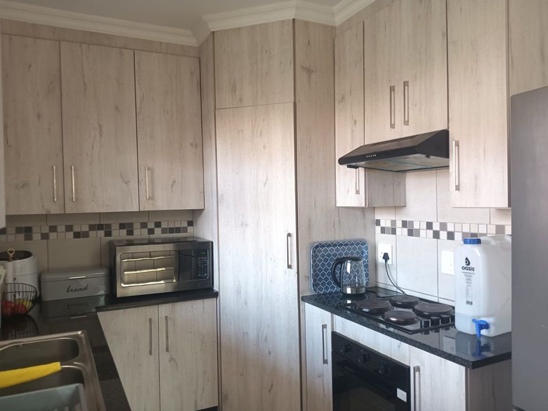 A well-maintained kitchen featuring light wood-grain laminate cabinetry, dark granite countertops, a built-in oven, electric hob, and a tiled backsplash.
