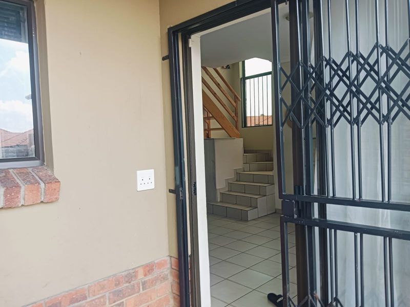 View of the townhouse entrance featuring a security gate, tiled flooring, and an internal staircase with a wooden handrail.