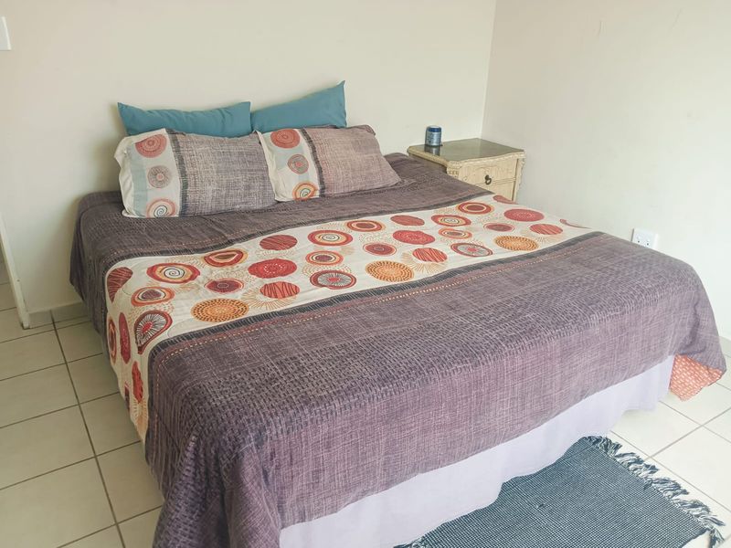 A simple bedroom featuring neutral walls and tiled flooring, providing a functional and clean space for rest.