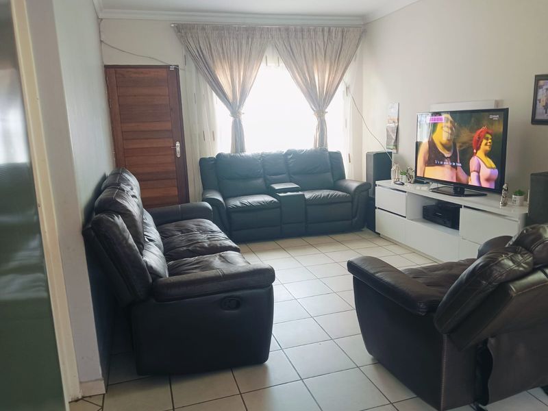 A functional living room featuring tiled flooring, a wooden door, and coved ceiling details, providing a comfortable space for relaxation.
