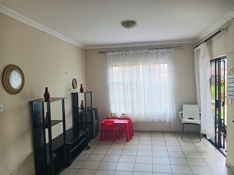A living room featuring tiled flooring, neutral walls, and a security gate leading to the exterior, providing a functional and well-lit living space.