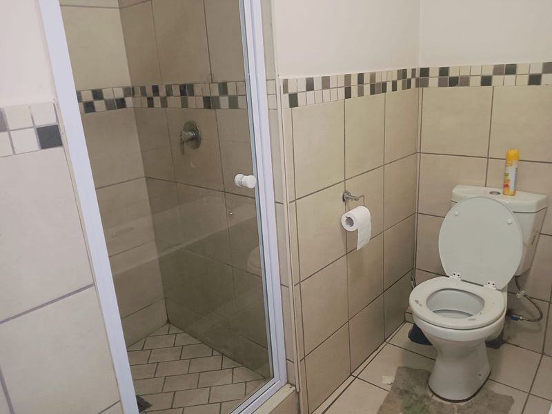 A functional bathroom featuring a glass-enclosed shower, standard toilet, and neutral wall tiling with a decorative accent border.