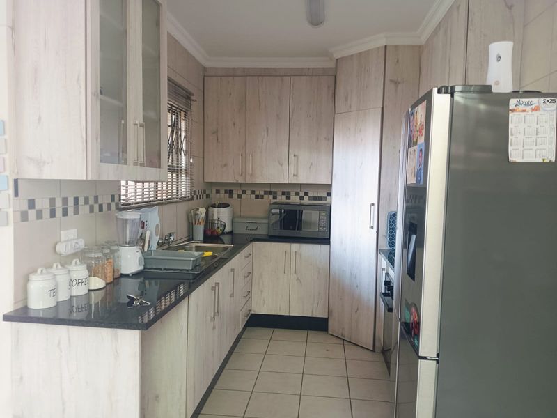 A functional kitchen featuring light wood-grain laminate cabinetry, dark granite countertops, a tiled backsplash, and ceramic floor tiles.