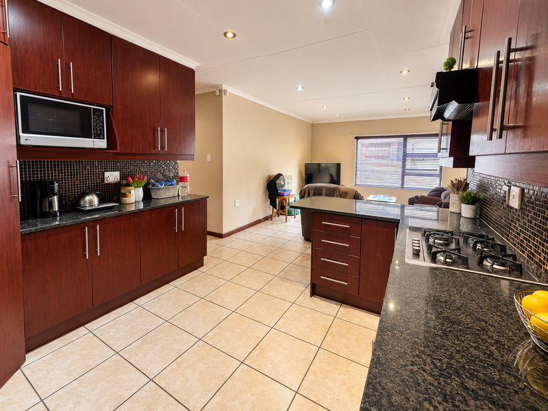 Open-plan kitchen featuring dark wood cabinetry, granite countertops, gas hob, and mosaic backsplash, flowing into a living area with tiled flooring throughout.