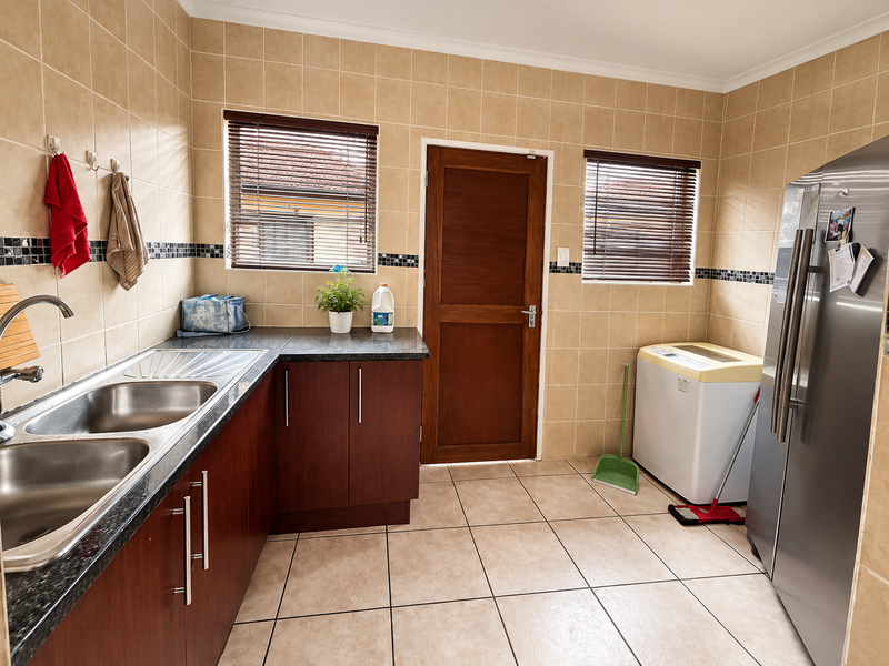 A functional laundry room featuring tiled walls and flooring, built-in cabinetry with laminate countertops, and a double stainless steel sink.