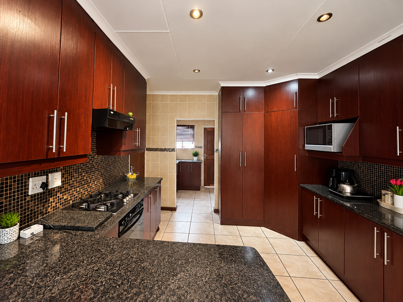 A well-maintained kitchen featuring dark wood cabinetry, granite countertops, a gas hob, and built-in appliances, with a tiled backsplash and flooring.