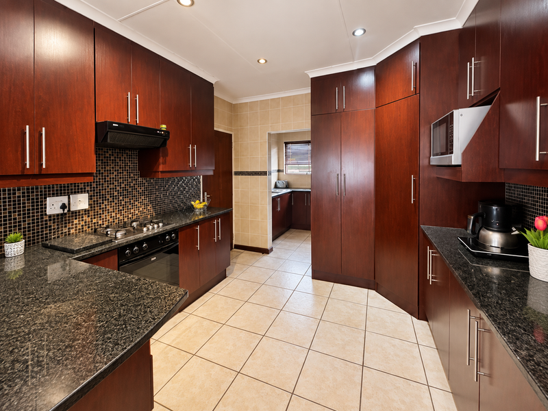 A well-maintained kitchen featuring dark wood cabinetry, granite countertops, a gas hob, built-in oven, and a tiled backsplash, with an adjoining scullery area.