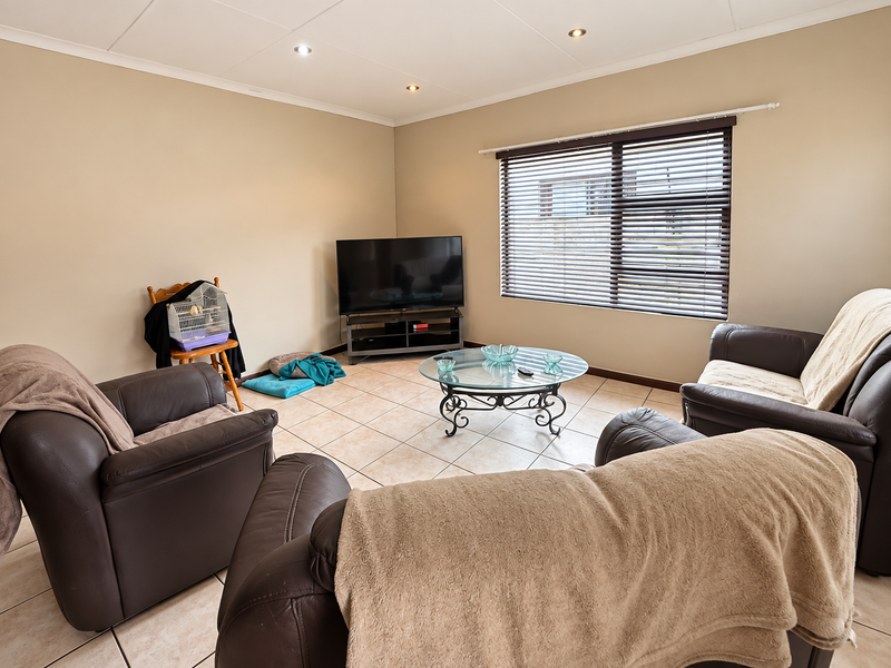 A comfortable living room featuring neutral wall tones, tiled flooring, and large windows fitted with venetian blinds, providing a bright and functional space.