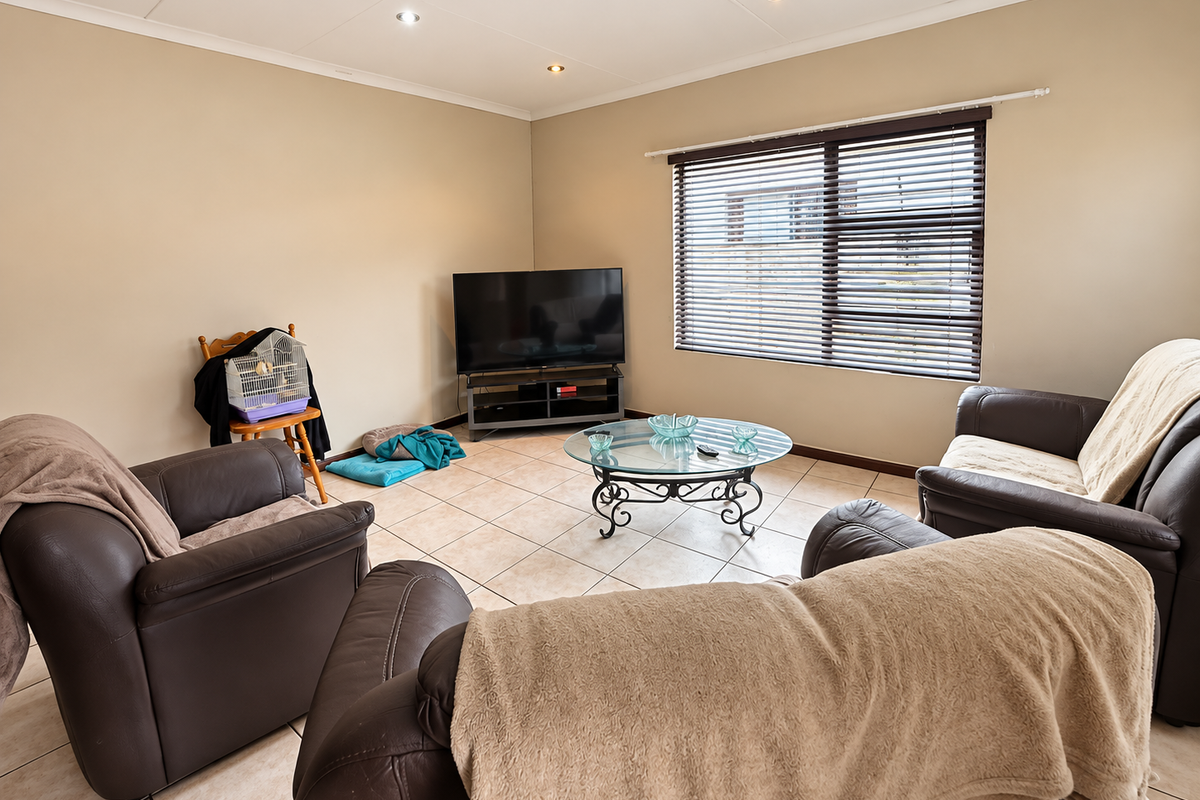 A comfortable living room featuring neutral wall tones, tiled flooring, and large windows fitted with venetian blinds, providing a bright and functional space.