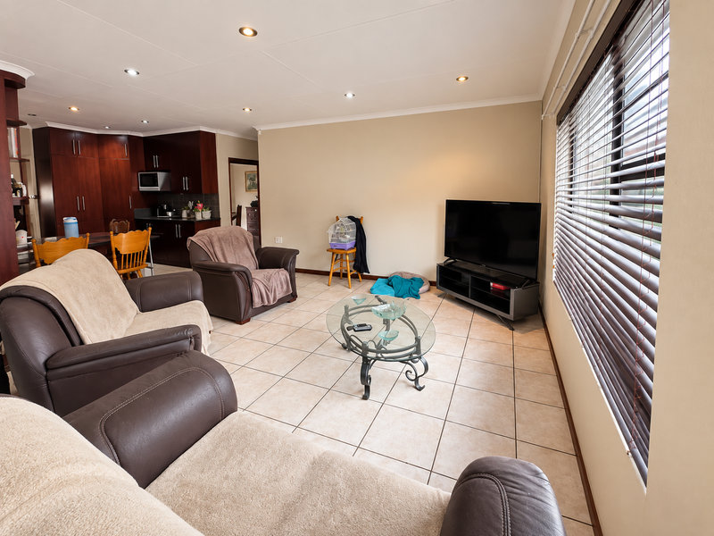 Open-plan living area featuring tiled flooring, recessed downlights, and venetian blinds, seamlessly connected to a kitchen with dark wood cabinetry.