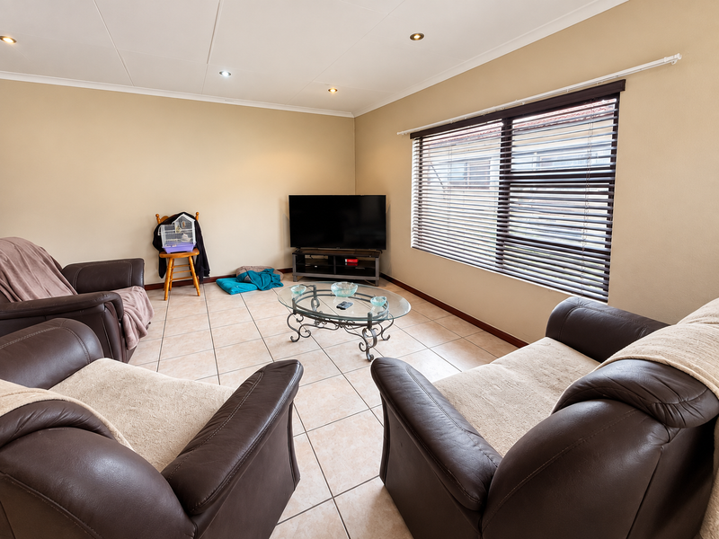 A comfortable living room featuring neutral tiled flooring, recessed downlighting, and large windows fitted with venetian blinds.