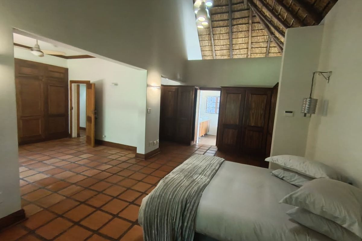 Spacious bedroom featuring a high vaulted thatched ceiling, terracotta tiled flooring, and extensive built-in wooden cabinetry with an adjoining en-suite bathroom.