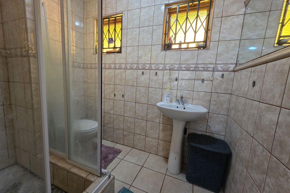 A functional bathroom featuring a pedestal basin, shower enclosure, and fully tiled walls and floors, requiring cosmetic updates to modernize the space.