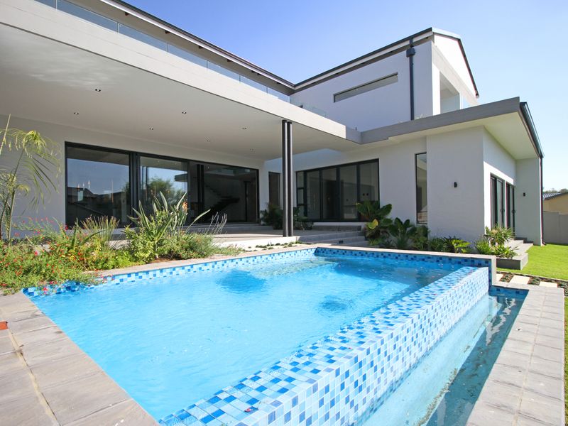 Modern outdoor living area featuring a tiled swimming pool, spacious covered patio, and seamless indoor-outdoor flow through large sliding glass doors.