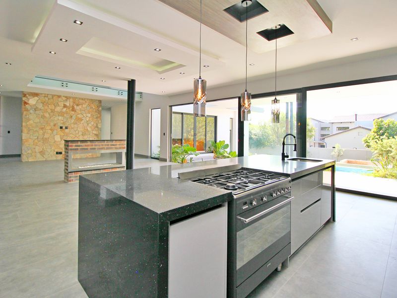 Spacious open-plan living area featuring a modern kitchen island with gas cooktop, stone feature wall, double-sided fireplace, and large sliding doors to the patio.