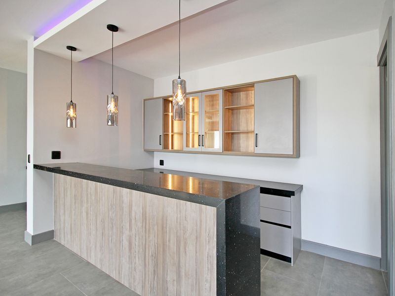 Modern built-in bar area featuring a stone countertop, sleek cabinetry with integrated lighting, and contemporary pendant fixtures in a clean, minimalist space.
