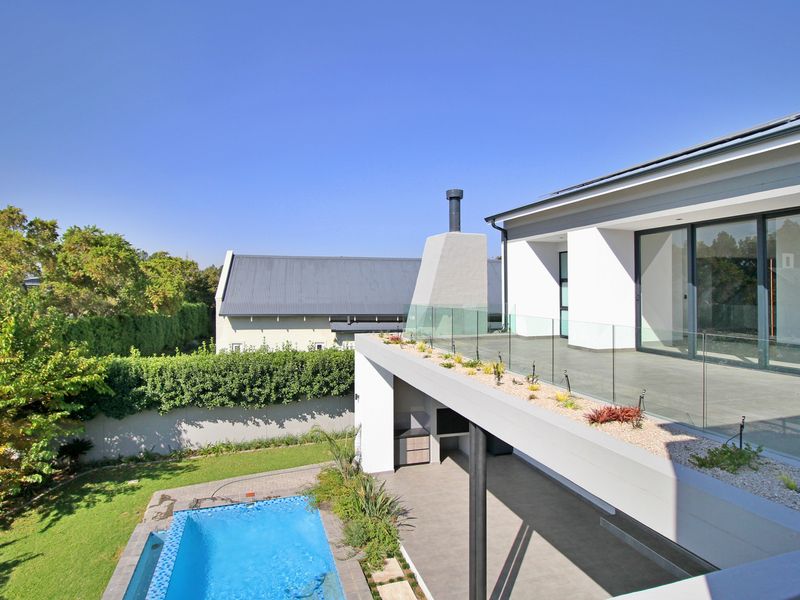 Modern rear exterior featuring a swimming pool, covered patio with built-in braai, and an elevated terrace with glass balustrades.