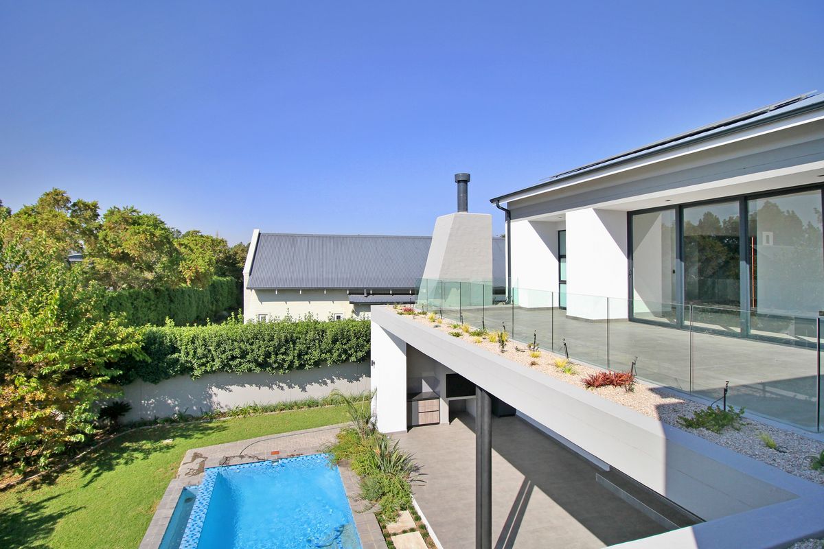 Modern rear exterior featuring a swimming pool, covered patio with built-in braai, and an elevated terrace with glass balustrades.