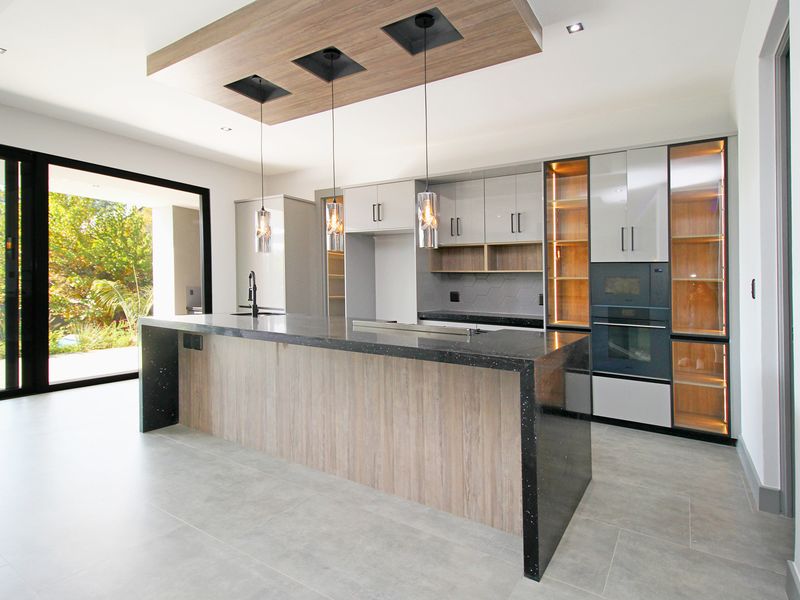 Modern kitchen featuring a large island with stone countertops, integrated cabinetry, built-in oven, and seamless access to the outdoor patio through sliding glass doors.